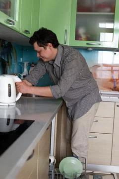 Young man doing homework in the kitchen. Washing dishes in a dishwasher. Dad  Stock Photos
