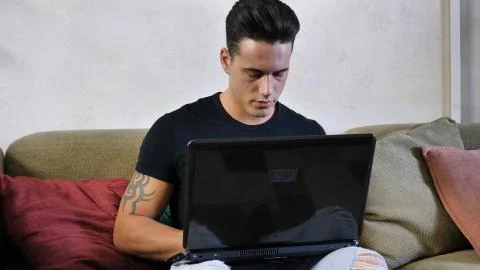 Young Man Doing Homework on Laptop on Couch Stock Photos