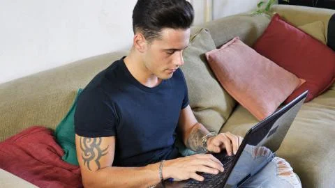 Young Man Doing Homework on Laptop on Couch Stock Photos