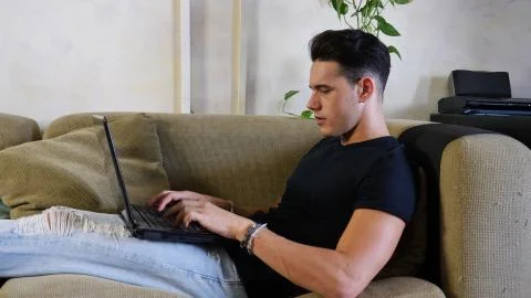 Young Man Doing Homework on Laptop on Couch Stock Photos