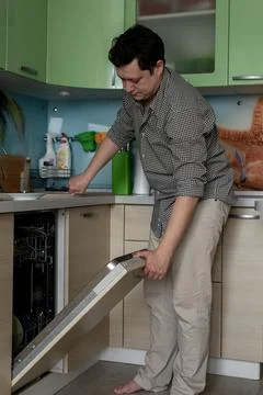 Young man doing homework. Puts the dishes in the dishwasher for washing. Dail Stock Photos