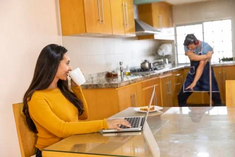 Young man doing housework while his wife is having fun on the computer . Stock Photos