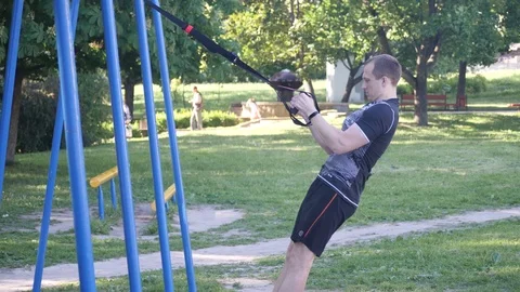 Young man doing intense pull-ups on fitness stripes in a summer park. 4K slow mo Stock Footage 99386680