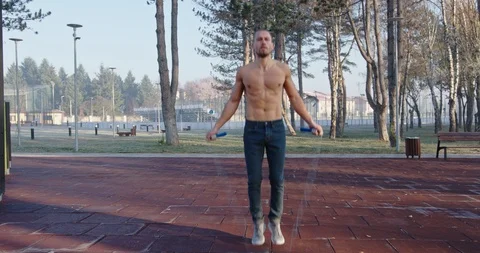 Young man doing jump rope exercise in public park Stock Footage 121715266