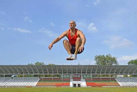 A young man doing a jump up workout on the green lawn of the city stadium Stock Photos