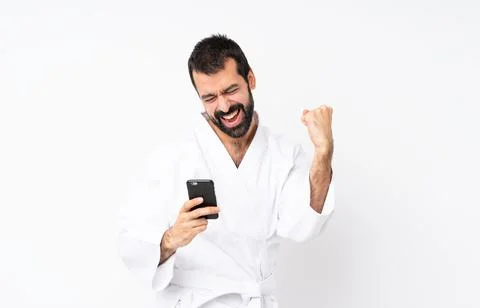 Young man doing karate over isolated white background with phone in victory p Stock Photos