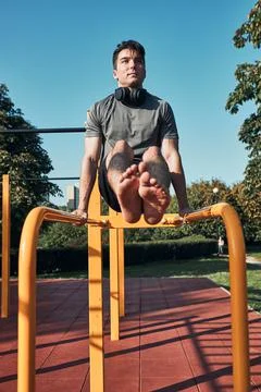 Young man doing L-Sit on parallel bars during his workout in a modern calisth Stock Photos
