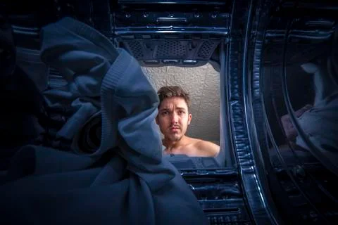 Young man doing laundry View from the inside of broken washing machine Foto stock