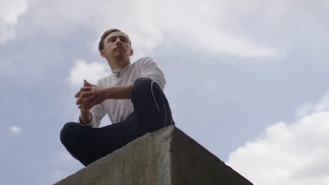 Young man doing parkour stops at the edge of a building before leaping off, in s Stock Footage 94302004
