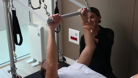 Young man doing pilates exercise in reformer bed with his female instructor Stock Footage 142523573