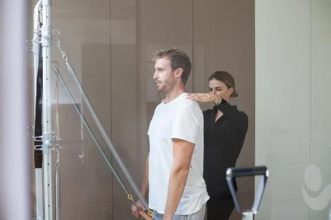 Young man doing pilates exercise on reformer with his female instructor Foto stock