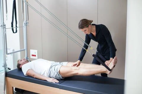Young man doing pilates exercise on reformer with his female instructor Stock Photos