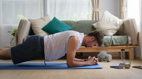 Young man doing plank exercise and watching online tutorial on computer lapto Stock Photos