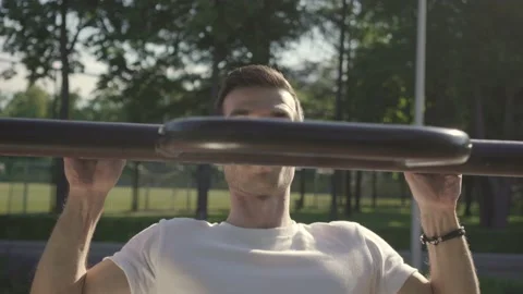 Young man doing pull-ups on horizon bar on sports ground Stock Footage 146305006