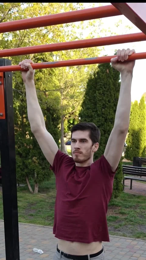 Young man doing pull-ups on an outdoor fitness bar during summer Stock Footage 312299267