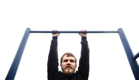 Young man doing pull ups on horizontal bar outdoors Stock Photos