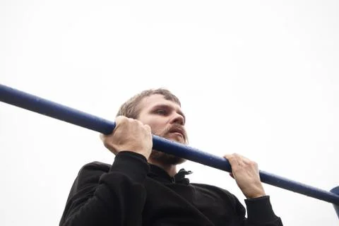 Young man doing pull ups on horizontal bar outdoors Stock Photos