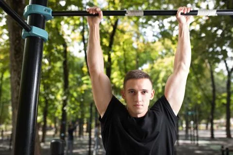 Young man doing pull ups on horizontal bar outdoors, workout, sp Stock Photos