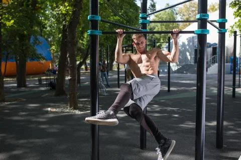 Young man doing pull ups on horizontal bar outdoors, workout, sp Stock Photos