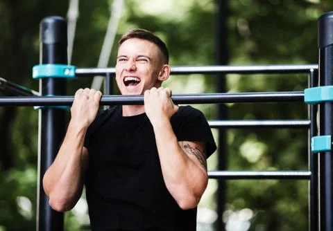 Young man doing pull ups on horizontal bar outdoors, workout, sp Stock-Fotos