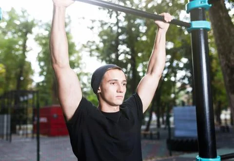 Young man doing pull ups on horizontal bar outdoors, workout, sp Stock Photos