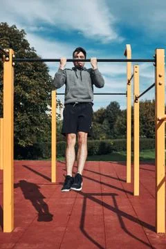 Young man doing pull-ups during his workout in a modern calisthenics street w Stock Photos