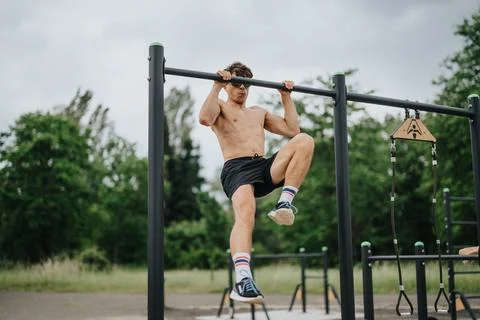 Young man doing pull-ups on parallel bars in outdoor gym for fitness training 写真素材