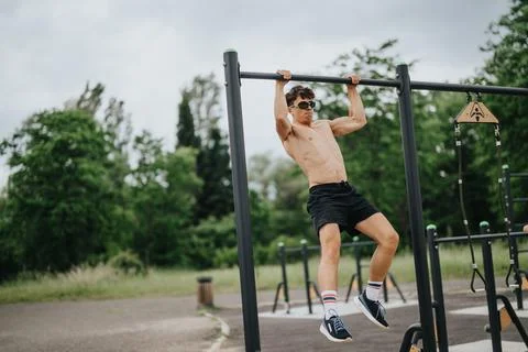 Young man doing pull-ups on outdoor parallel bars in a park Stock-Fotos