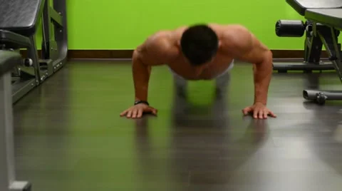 Young man doing push ups facing the camera in front of green wall Stock Footage