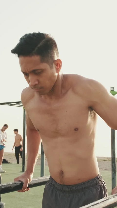 Young man doing push-ups on parallel bars on a sports ground by the sea 스톡 동영상 245591002