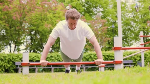 Young man doing push-ups on a bar at an outdoor sports ground. Fit guy training  Stock Footage 336686820