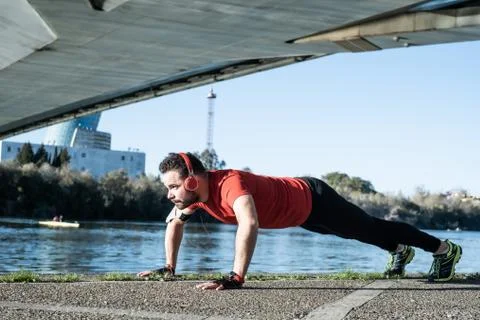 Young man doing push-ups with a red t-shirt and music headphones, in an urban Stock Photos