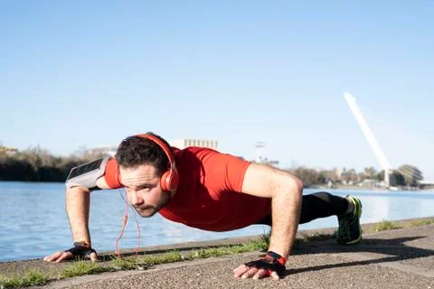 Young man doing push-ups with a red t-shirt and music headphones, in an urban Stock Photos