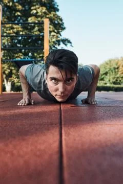 Young man doing push-ups on a red rubber ground during his workout in a moder Stock Photos