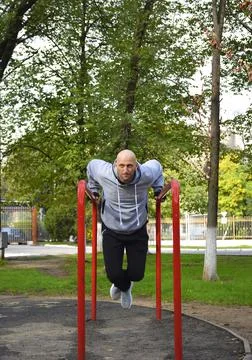 A young man is doing push-ups on the uneven bars. Street workout. Medium shot Stock Photos