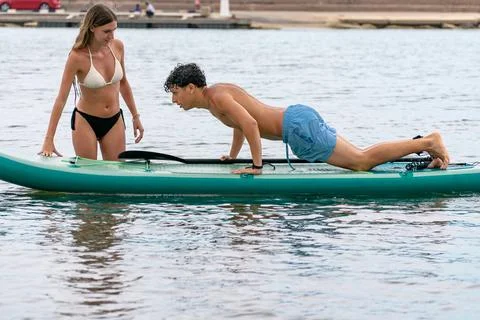 Young man doing push-ups on paddle board with girlfriend watching Stock Photos
