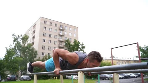 Young man is doing shuttle push-ups on parallel bars outdoors Stock Footage 114089549