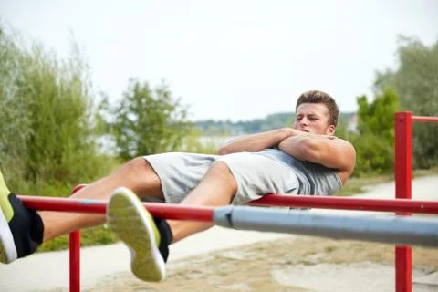 Young man doing sit up on parallel bars outdoors Stock Photos