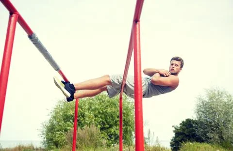 Young man doing sit up on parallel bars outdoors Stock Photos