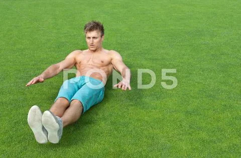 Young man doing sit-ups on sports field Stock Photos