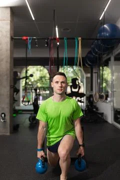 A young man doing split squat, and holding the kettlebells Stock Photos