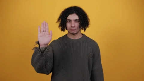 Young man doing stop gesture with hand over isolated yellow background. Curly 스톡 동영상 260566719
