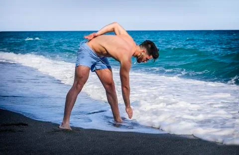 Young man doing stretching exercise on beach Stock Photos
