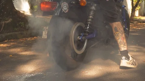 Young man doing a tire burnout on motorcycle on the road at sunset slow motion Stock Footage 105372828