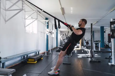 Young man doing TRX exercises at the gym. TRX training. Sport and fitness. Cr Stock Photos