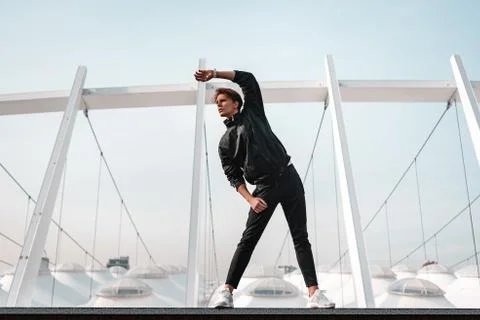 Young man is doing warming up exercises near the stadium Stock Photos