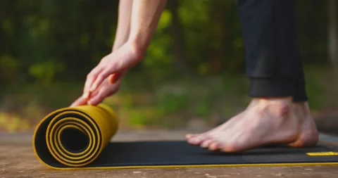 Young man doing yoga exercise - opening his yellow yoga mat in park. Close-up Stock Footage 157992209