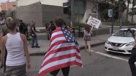 A Young Man Draped in a U.S. Flag Approaches a Anti-Trump Rally Video stock 225215394