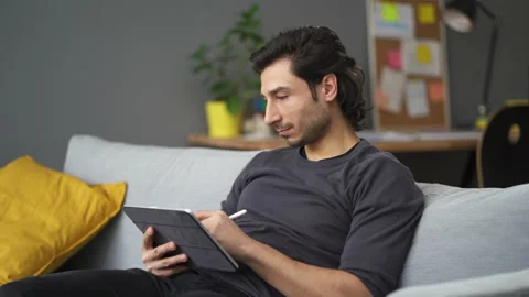 Young man drawing with digital tablet sitting on the sofa at home Stock Footage 149247326