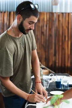 Young man drawing on table full of work tools during fine arts class. Vertical Stock Photos